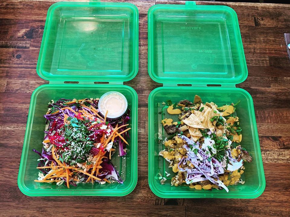 two reusable green takeout boxes filled with food on a table