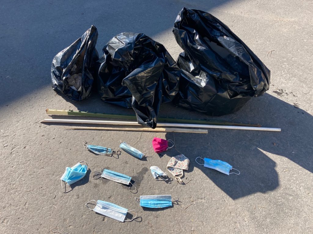 ten collected disposable face masks laying on pavement in front of two filled garbage bags